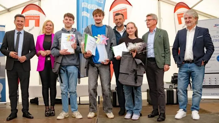 Mehrere Menschen halten Urkunden und einen Pokal in die Kamera 