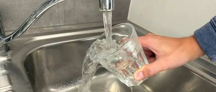 Eine Person hält ein Glas unter einen laufenden Wasserhahn.