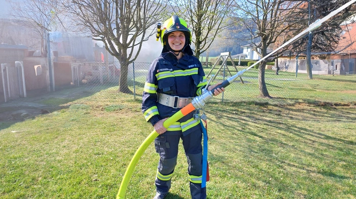 Eine Feuerwehrfrau hält einen Wasserschlauch in den Händen und lächelt in die Kamera.