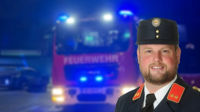 Ein Feuerwehrauto im Hintergrund mit Blaulicht. Vorne ein Feuerwehrmann in Uniform 