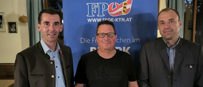 Drei Männer posieren vor einem FPÖ-Plakat für ein Foto.