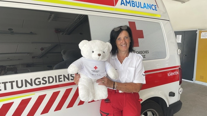 Eine Frau steht vor einem Rettungsauto und hält einen Teddybären in der Hand 