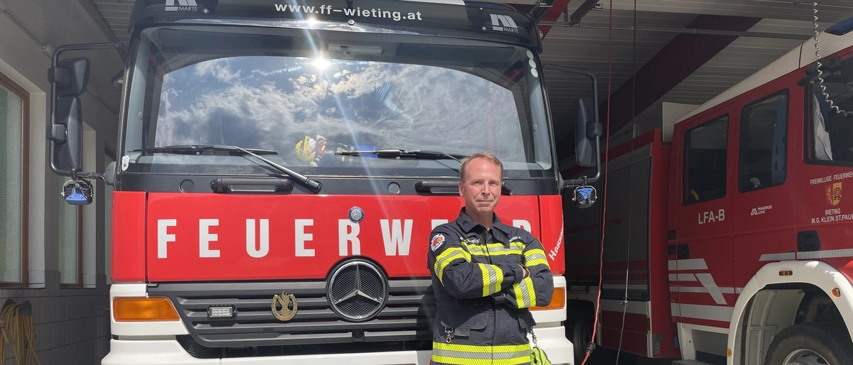 Ein Mann steht mit verschränkten Armen vor einem Feuerwehrauto 