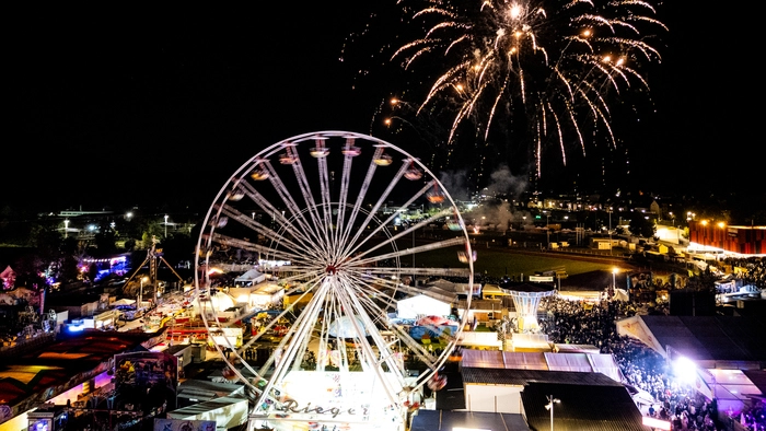 Foto eines Volksfestes bei Nacht. In der Luft explodiert eine Silvesterrakete
