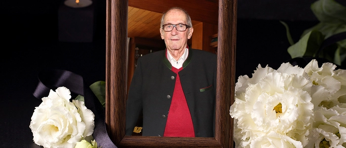 Ein Foto in einem schwarzen Rahmen, daneben ein Trauerbouquet.