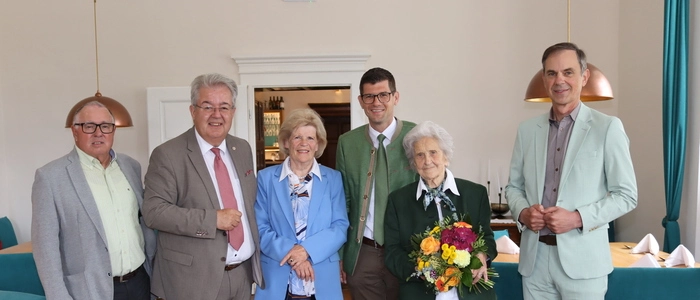 Sechs Menschen stehen in einer Reihe. Eine Dame hält einen Blumenstrauß