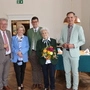 Sechs Menschen stehen in einer Reihe. Eine Dame hält einen Blumenstrauß 