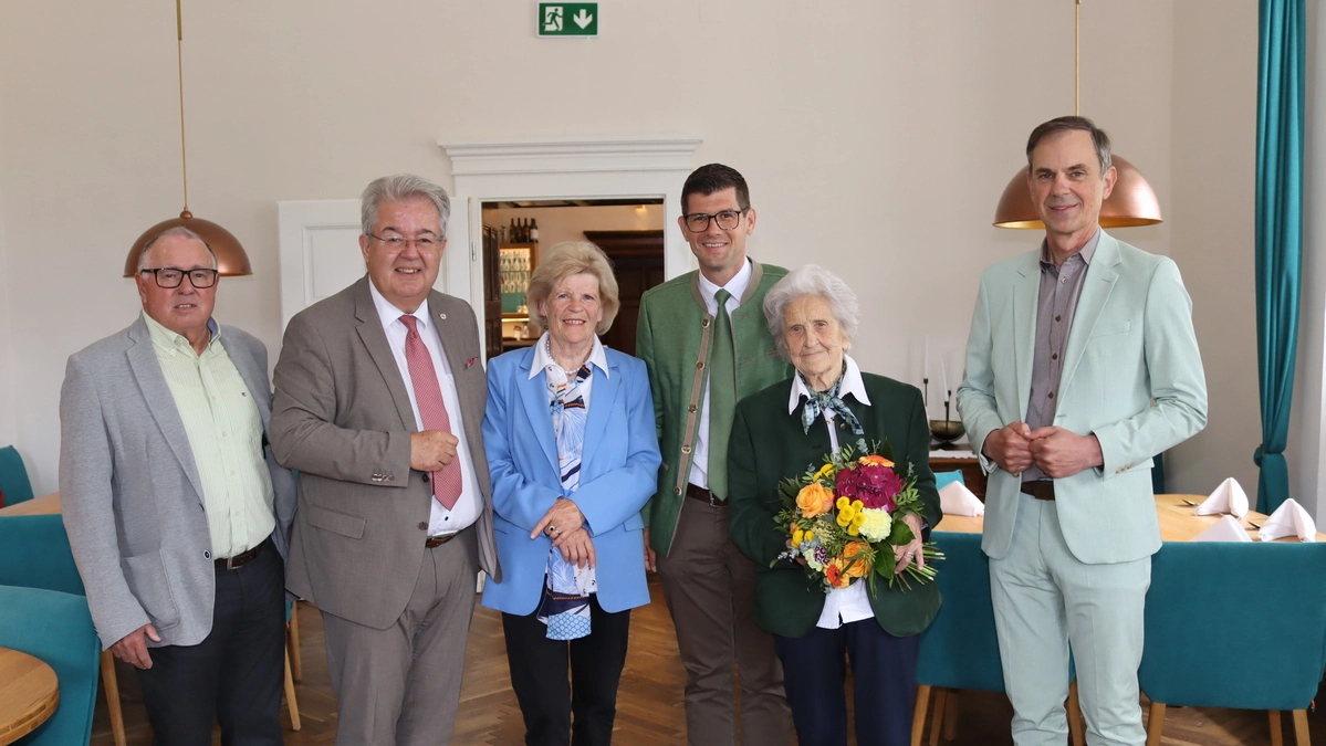 Sechs Menschen stehen in einer Reihe. Eine Dame hält einen Blumenstrauß 