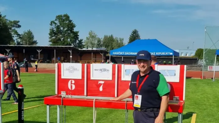 Ein Mann steht bei sonnigem Wetter auf einem Sportplatz und lächelt in die Kamera.