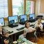 Vier PCs stehen eingeschaltet nebeneinander auf Tischen. Davor sitzen junge Volksschülerinnen und -schüler und lächeln in die Kamera | Schülerinnen und Schüler der Volksschule Globasnitz/Globasnica mit den gespendeten PCs