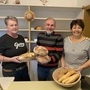 Bäckermeister Manfred Greiner steht, flankiert von seinen beiden Verkäuferinnen Vera und Renate, mit zwei Broten in der Hand im Verkaufsraum seiner Bäckerei. Die Regale hinter ihm sind schon ziemlich leer, da das Geschäft in wenigen Tagen schließt | Bäckermeister Manfred Greiner mit seinen Verkäuferinnen Vera (links) und Renate 