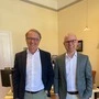 Die beiden Notare Reinhard Kern und Armin Müller stehen in Kerns Büro nebeneinander im Anzug und lächeln in die Kamera