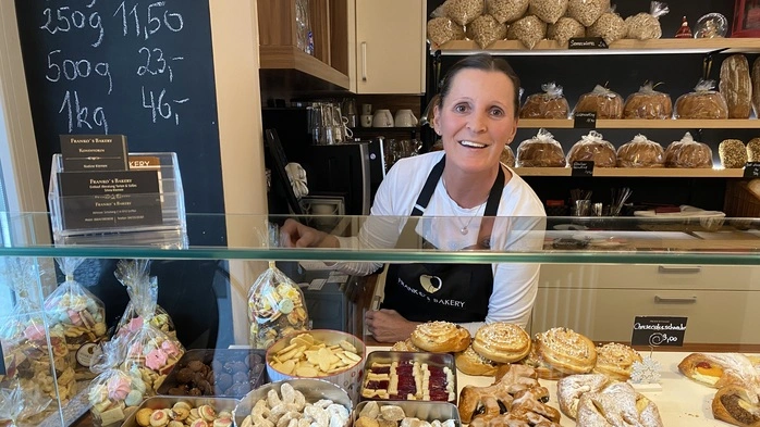 Chefin Silvia Klemen von Franko‘s Bakery in Griffen steht hinter ihrer Verkaufsvitrine, in der man Weihnachtskekse in Dosen und anderes Gebäck sieht. Hinter ihr ist ein Regal voller Brot | Chefin Silvia Klemen von Franko‘s Bakery in Griffen mit ihren Weihnachtskeksen in der Vitrine