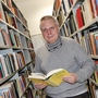 Allgemeinmediziner und Wissenschaftler Michael Schüller steht mit einem Buch in der Hand zwischen zwei Bücherregalen