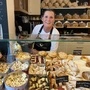 Chefin Silvia Klemen von Franko‘s Bakery in Griffen steht hinter ihrer Verkaufsvitrine, in der man Weihnachtskekse in Dosen und anderes Gebäck sieht. Hinter ihr ist ein Regal voller Brot | Chefin Silvia Klemen von Franko‘s Bakery in Griffen mit ihren Weihnachtskeksen in der Vitrine