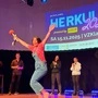 Die Völkermarkter Kabarettistin steht auf der Bühne im Veranstaltungszentrum Klagenfurt. Sie hat die Hände in die Luft gestreckt, in einer Hand hält sie eine Sektflasche und einen Klobesen. Rundherum stehen die anderen Finalisten und klatschen. | Katrin Winkler-Jandl im Freudentaumel nach dem Gewinn des ‚Herkules 2025‘
