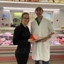 Fleischermeister Simon Čebul und seine Lebensgefährtin Yvonne Lessiak stehen vor der Fleischtheke im Geschäft. Sie ist ganz in Schwarz gekleidet, trägt eine Brille und hält eine Extrawurst in den Händen, er trägt eine weiße Kappe und einen weißen Arbeitsmantel und hält eine Salami | Fleischermeister Simon Čebul mit seiner Lebensgefährtin Yvonne Lessiak