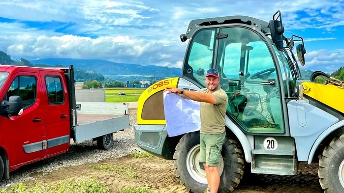 Unternehmer Stefan Krenn steht vor einem Bagger und hält einen Plan in der Hand