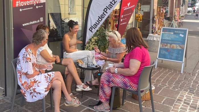 Fünf Frauen sitzen um einen kleinen Tisch vor einem Geschäft in St. Veit und reden miteinander.
