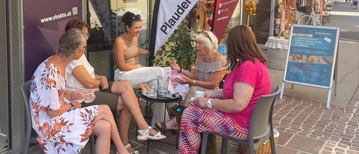Fünf Frauen sitzen um einen kleinen Tisch vor einem Geschäft in St. Veit und reden miteinander.