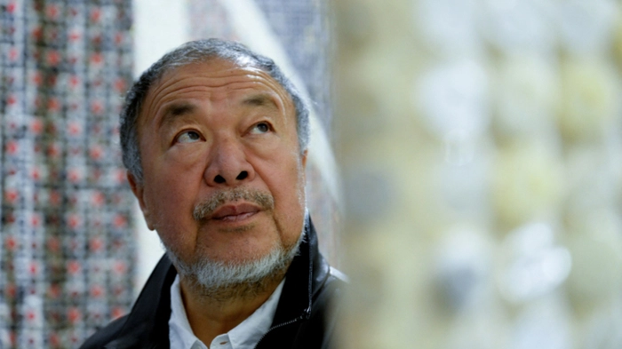 Chinese artist Ai Weiwei poses with one of his new works entitled 'Eight-Nation Alliance Flags' during a photocall to promote his forthcoming exhibition 'Ai Weiwei: Button Up!', at the Aviva Studios in Manchester, northern England, on July 1, 2026. (Photo by Peter POWELL / AFP) / RESTRICTED TO EDITORIAL USE - MANDATORY MENTION OF THE ARTIST UPON PUBLICATION - TO ILLUSTRATE THE EVENT AS SPECIFIED IN THE CAPTION