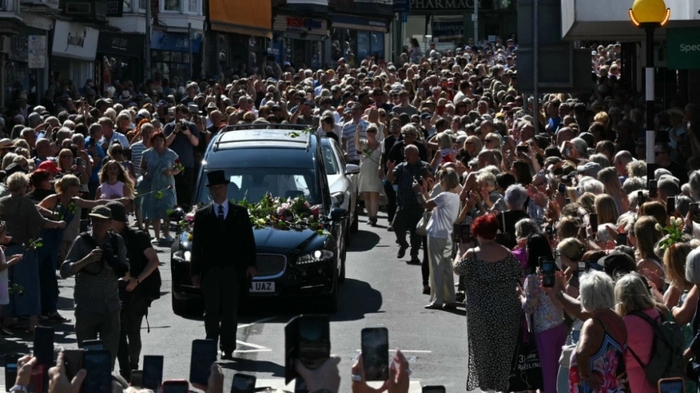 Mourners and fans line the streets to pay their respects as a hearse carrying the coffin of the late singer Bonnie Tyler is driven through her home town of Mumbles, southwest Wales, on August 15, 2026. Welsh singer Bonnie Tyler, best known for her powerful, haunting love song "Total Eclipse of the Heart" died in Portugal on July 8, 2026, aged 75. (Photo by JUSTIN TALLIS / AFP) / Correction - “The erroneous mention[s] appearing in the metadata of this photo by JUSTIN TALLIS has been modified in AFP systems in the following manner: [died in Portugal on July 8 2026,] instead of [died in Portugal on August 9, 2026,]. Please immediately remove the erroneous mention[s] from all your online services and delete it (them) from your servers. If you have been authorized by AFP to distribute it (them) to third parties, please ensure that the same actions are carried out by them. Failure to promptly comply with these instructions will entail liability on your part for any continued or post notification usage. Therefore we thank you very much for all your attention and prompt action. We are sorry for the inconvenience this notification may cause and remain at your disposal for any further information you may require.”