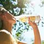 Bottom closeup view of a pretty blonde young woman enjoying drinking lemonade while resting in the park on sunlight. Female on a picnic having a detox drink.