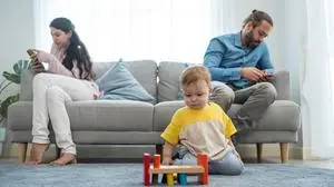 Caucasian phone addict parents don't pay attention with baby toddler. Family problem, Father and Mother sit on sofa and using cellphone ignore young infant boy son play alone on floor in living room.