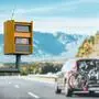 A radar-equipped speed camera monitors the traffic on a road, flashing a yellow light when it catches a car exceeding the speed limit, and using technology to identify the vehicle and enforce the law.