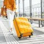 Young female traveler walking with a yellow suitcase at the modern transport stop outdoors, back view. Concept of an urban transportation and travel