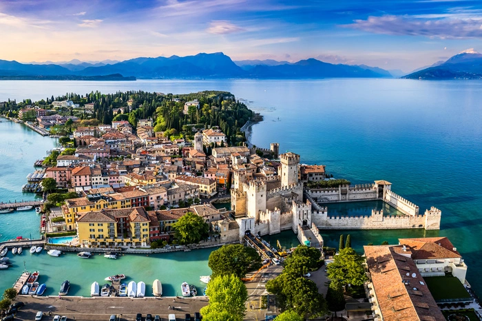 Sirmione. Am Südufer des Gardasees ist Sirmione nicht nur klimatisch begünstigt, auch seine Lage ist einzigartig. Der Ort liegt auf einer Halbinsel, die etwa vier Kilometer in den See hineinragt. Hoch über der Altstadt mit ihren Cafes und Restaurants thronen die Zinnen der märchenhaften Scaligerburg, gerne streifen Besucher über Reste einer römischen Villa – die „Grotten des Catull“ –, die einst ein Thermalbad war. Die heiße Quelle sprudelt bis heute und speist die Kureinrichtungen und Spas des Orts. 