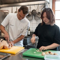 Haubenkoch Markus Sattler zerlegt den Hahn, die Autorin schneidet Pilze und Zwiebeln für die Sauce