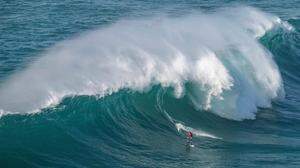 Ein Surfer reitet auf einer überschlagenden Welle im portugiesischen Nazaré