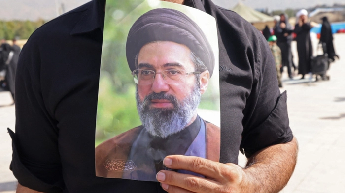 A mourner carries a portrait of Iran's supreme leader Mojtaba Khamenei, upon his arrival at the Grand Mosalla to attend the funeral ceremonies of slain supreme leader Ayatollah Ali Khamenei, in Tehran on July 4, 2026. Funeral ceremonies for Iran's supreme leader Ali Khamenei officially began on July 4, state television reported, an event drawing thousands and intended to serve as a show of strength to the Islamic republic's foes. (Photo by ATTA KENARE / AFP) /