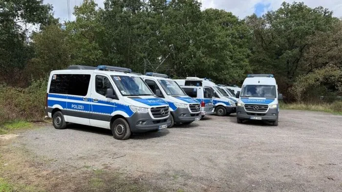 05.09.2026, Nordrhein-Westfalen, Niederzier: Polizeifahrzeuge stehen neben Strommasten, während die Polizei den Hambacher Forst in der Nähe von Niederzier durchsucht. Die Polizei fahndet weiter mit Hochdruck nach einem Mann, der Sabotageaktionen gegen das deutsche Stromnetz verübt haben soll. Foto: Jan Ohmen/dpa +++ dpa-Bildfunk +++