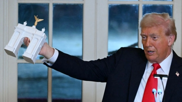 (FILES) US President Donald Trump holds up a model for a proposed "Independence Arch" as he speaks during a dinner with ballroom donors in the East Room of the White House in Washington, DC on October 15, 2025. A massive arch that Donald Trump wants to build on a historic location in Washington will double as a base for drones and snipers, the US president announced on September 20, 2026. (Photo by ANDREW CABALLERO-REYNOLDS / AFP)