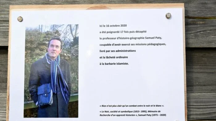 A photograph taken on October 16, 2023 shows a commemorative plaque for slain teacher Samuel Paty (portrait) near the Bois d'Aulne school in Conflans-Sainte-Honorine, outside Paris. France was set to hold tribute ceremonies for Samuel Paty, the history-geography teacher who was beheaded on October 16, 2020 for showing Mohammed cartoons during lessons on freedom of expression and French teacher Dominique Bernard, 57, who was stabbed to death at the school in Arras in what the government has described as an Islamist terror attack. (Photo by Bertrand GUAY / POOL / AFP)