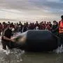 Migrants move a smuggling boat into the water as they embark on the beach of Gravelines, near Dunkirk, northern France on October 12, 2022, in an attempt to cross the English Channel. Since the beginning of the year, more than 33,500 people have already made the perilous crossing of the English Channel, one of the busiest shipping lanes in the world, where more than 400 commercial ships pass each day. (Photo by Sameer Al-DOUMY / AFP)