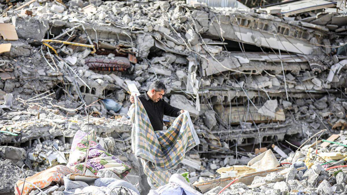 Ein Mann durchsucht die Trümmer eines völlig zerstörten Hauses  | Die Stadt Adiyaman wurde schwer getroffen von dem Erdbeben im letzten Februar 