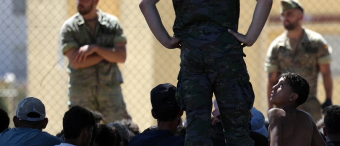 A young migrant looks at a member of the Spanish Army's 'Regulares' infantry force near the border post, prior to escorting them back to Morocco, in the Spanish enclave of Ceuta on August 2, 2026. At least 72 people died during last week's mass influx of migrants into Spain's Ceuta enclave, when tens of thousands of people mostly swam around the border post from Morocco, local officials said today. Most of the estimated 60,000 people who rushed into Spain's north African territory have returned to Morocco since the territory's largest mass migrant crossing. (Photo by Henry NICHOLLS / AFP)