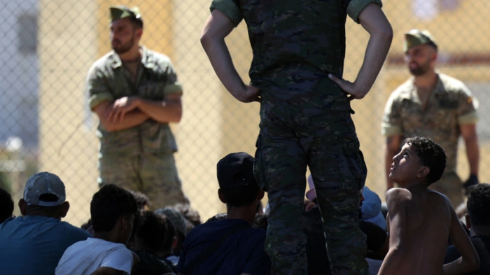 A young migrant looks at a member of the Spanish Army's 'Regulares' infantry force near the border post, prior to escorting them back to Morocco, in the Spanish enclave of Ceuta on August 2, 2026. At least 72 people died during last week's mass influx of migrants into Spain's Ceuta enclave, when tens of thousands of people mostly swam around the border post from Morocco, local officials said today. Most of the estimated 60,000 people who rushed into Spain's north African territory have returned to Morocco since the territory's largest mass migrant crossing. (Photo by Henry NICHOLLS / AFP)