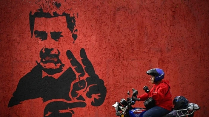 (FILES) A motorcyclist rides past a mural of ousted Venezuela's President Nicolas Maduro flashing the V sign, in Caracas, on May 14, 2026. Eight months after US forces captured Venezuelan President Nicolas Maduro on January 3, 2026, the prevailing national mood is bittersweet as delight at his fall gives way to impatience about ongoing economic hardship. (Photo by Federico PARRA / AFP)
