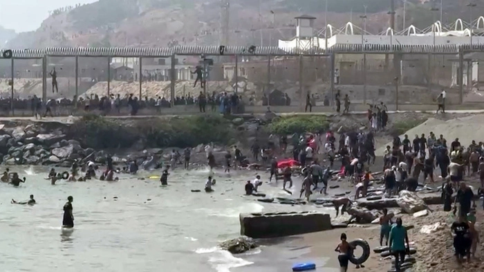 This video frame grab obtained from an AFP video shows migrants reaching the shore of Spanish north African exclave of Ceuta, after swimming around the border fence between Morocco and Spain, in Ceuta on July 30, 2026. Hundreds of migrants entered the Spanish north African exclave of Ceuta today, AFP reporters saw, many of them having swum by sea around the frontier fence. Migration from Morocco into Spain's two north African territories, Ceuta and Melilla, has long been a politically sensitive issue between the two countries, as thousands cross the border at times. AFP reporters saw a stream of adults and children, most of them wet, entering the town. (Photo by LucÌa DIAZ / AFP)