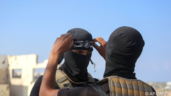 A Palestinian militant fighter of the Ezzedine al-Qassam Brigades, the armed wing of the Palestinian Hamas movement, fixes the headband of the group on his comrade's forehead as vehicles of the International Committee of the Red Cross (ICRC) (not pictured) transport the second batch of released Israeli hostages in the south of Deir el-Balah in the central Gaza Strip, on October 13, 2025. (Photo by Bashar TALEB / AFP)