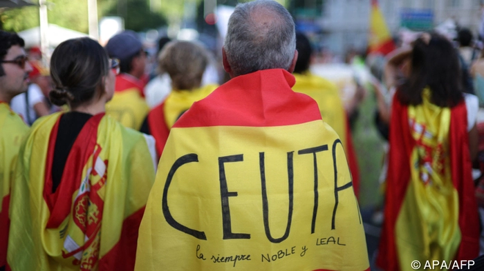 A protester is wrapped in a Spanish flag reading 'Ceuta always noble and loyal' during a demonstration one month after a mass influx of migrants in Ceuta, in front of the Spanish Parliament in Madrid, on September 2, 2026. Local anger divide Ceuta one month after the mass influx of migrants into the North African Spanish territory. 5,000 migrants according to the government, or at least 10,000, according to Ceuta authorities, remain in the small territory of 18.5 square kilometers and 80,000 inhabitants, wandering the streets in search of food and sleeping in streets and on beaches. (Photo by Thomas COEX / AFP)