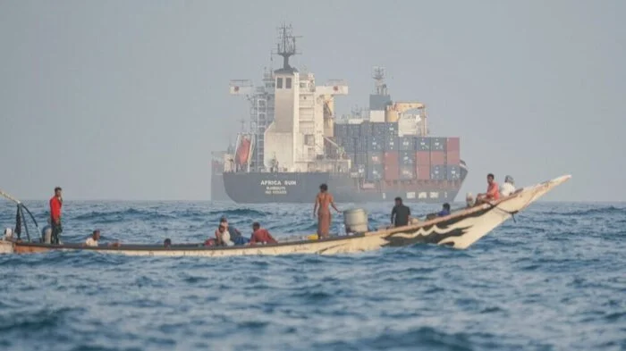 People sail their boat past container ships anchoring near the Strait of Bab al-Mandeb off Yemen's coast in the Gulf of Aden on August 6, 2026. (Photo by AFP) /