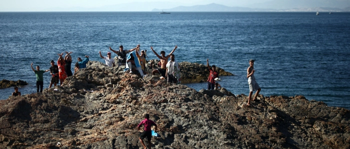 A group of migrants wave from the coastal rocks near the border post of the Spanish enclave of Ceuta on August 2, 2026. At least 72 people died during last week's mass influx of migrants into Spain's Ceuta enclave, when tens of thousands of people mostly swam around the border post from Morocco, local officials said today. Most of the estimated 60,000 people who rushed into Spain's north African territory have returned to Morocco since the territory's largest mass migrant crossing. (Photo by Henry Nicholls / AFP)