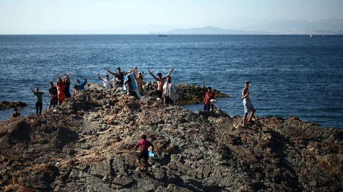 A group of migrants wave from the coastal rocks near the border post of the Spanish enclave of Ceuta on August 2, 2026. At least 72 people died during last week's mass influx of migrants into Spain's Ceuta enclave, when tens of thousands of people mostly swam around the border post from Morocco, local officials said today. Most of the estimated 60,000 people who rushed into Spain's north African territory have returned to Morocco since the territory's largest mass migrant crossing. (Photo by Henry Nicholls / AFP)