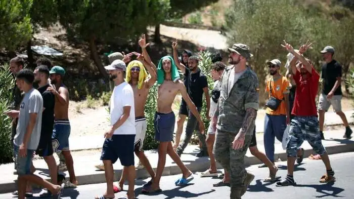 A group of migrants make their way back to Morocco from the short-stay centre CETI towards the border post, escorted by Spanish infantry soldiers, in the Spain's north African enclave of Ceuta, on August 2, 2026. At least 72 people died during the mass influx in recent days of migrants into Spain's Ceuta enclave, when tens of thousands of people mostly swam around the border post from Morocco, local officials said today. Most of the estimated 60,000 people who rushed into Spain's north African territory have returned to Morocco since the territory's largest mass migrant crossing. (Photo by Henry NICHOLLS / AFP)