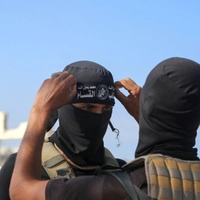 A Palestinian militant fighter of the Ezzedine al-Qassam Brigades, the armed wing of the Palestinian Hamas movement, fixes the headband of the group on his comrade's forehead as vehicles of the International Committee of the Red Cross (ICRC) (not pictured) transport the second batch of released Israeli hostages in the south of Deir el-Balah in the central Gaza Strip, on October 13, 2025. (Photo by Bashar TALEB / AFP)
